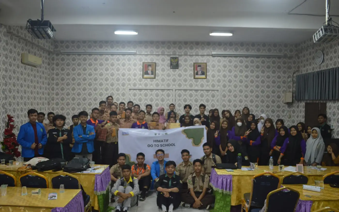 A hall at SMK Labor at the end of the seminar. Around fifty
            vocational students and the volunteer team stand behind a banner
            reading HIMATIF Go To School.