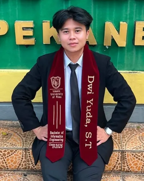 Dwi Yuda in a dark suit, wearing a maroon graduation stole
            reading Bachelor of Informatics Engineering, Class of 2026, in
            front of a Pekanbaru sign.