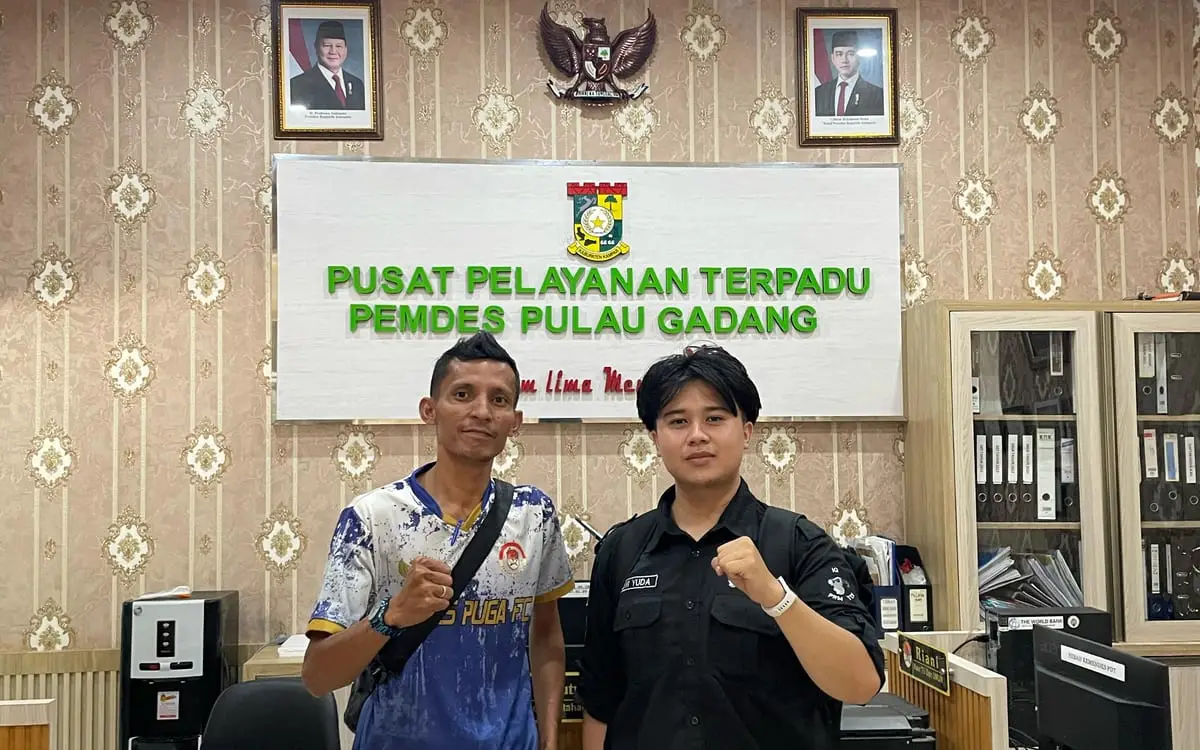 Standing with a member of village staff in the Pulau Gadang
                integrated service office, under the office's name board.